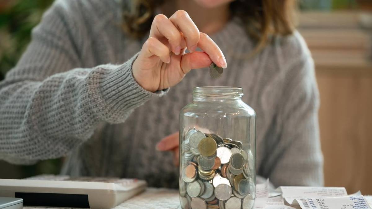 Person putting coins into a glass savings jar Person putting coins into a glass savings jar